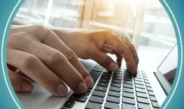 Hands typing on a laptop keyboard with sunlight streaming through a window in the background.